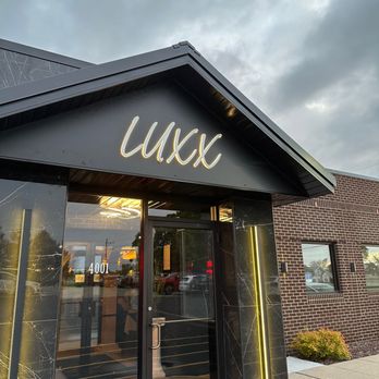 "Entrance of a modern black building with illuminated 'LUXX' signage above the door, vertical light fixtures, marble-like paneling, and address number 4001 on the glass door."